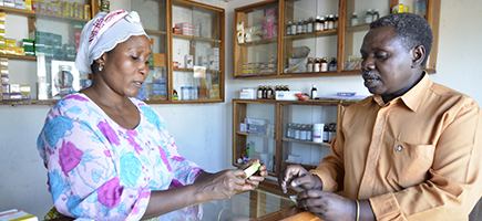A woman in colourful clothing sells a man a medicine.